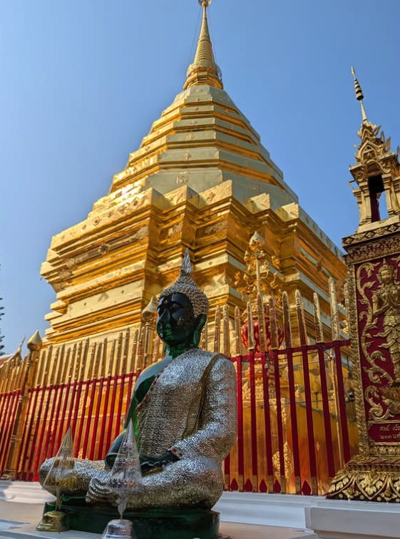 A bronze Buddha seated in front of the gilded chedi at Wat Phra That Doi Suthep